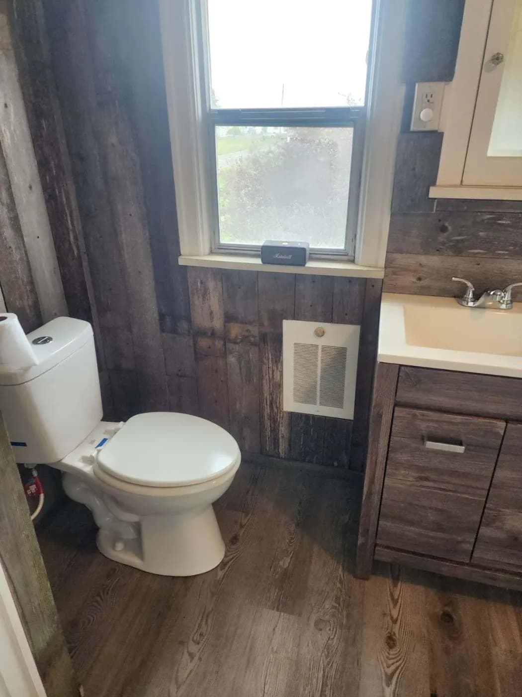 Restored bathroom with dark wood flooring, wood-paneled walls, white toilet and a wooden vanity