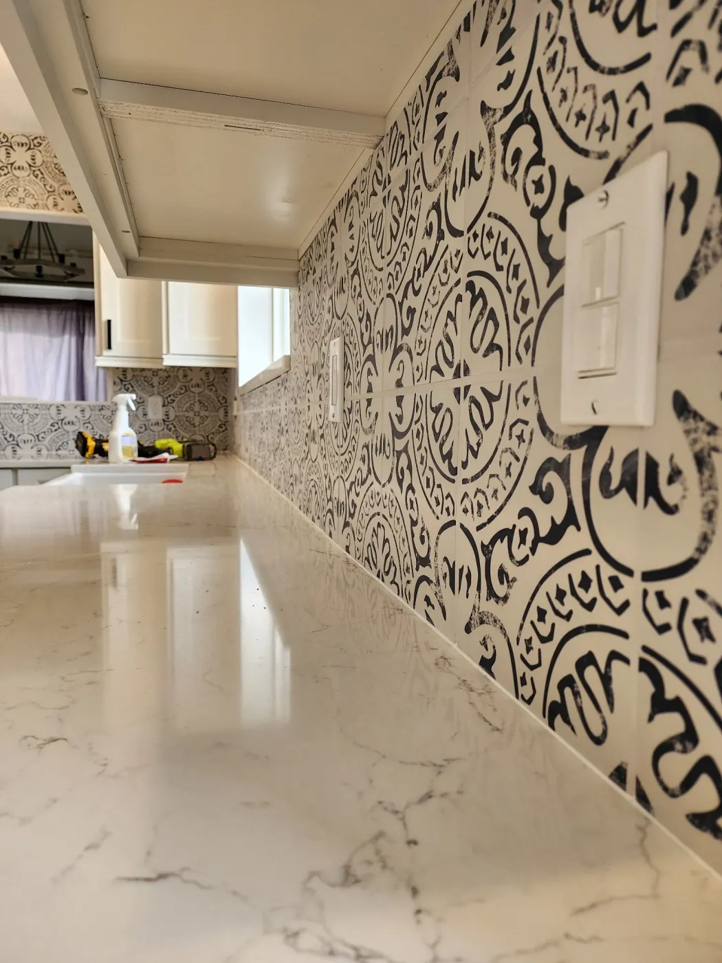 Kitchen with a black ornate patterned tile backsplash, marble flooring, white cabinetry and recessed lighting