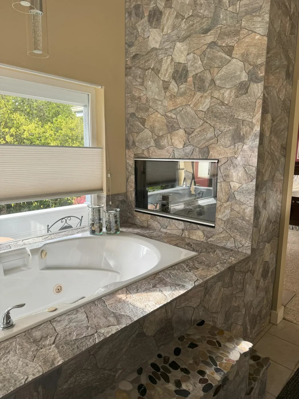 Master bathroom with stacked stone walls, white soaking tub, granite counters and river rock floor accents