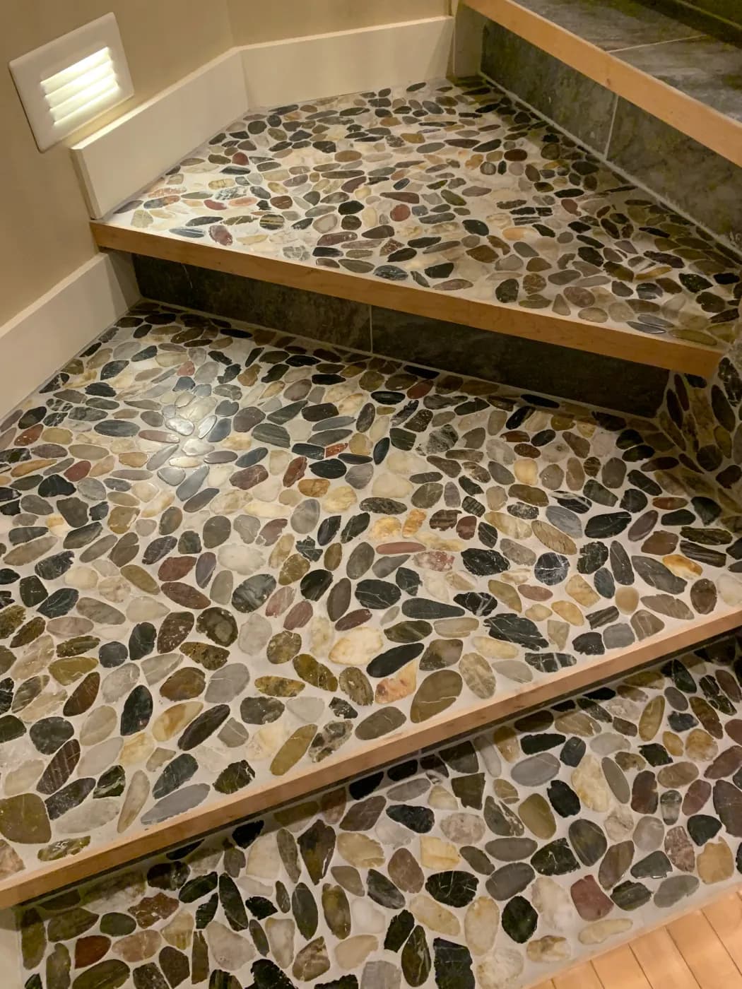 Multi-level pebble tile shower with natural stone flooring and wood trim framing