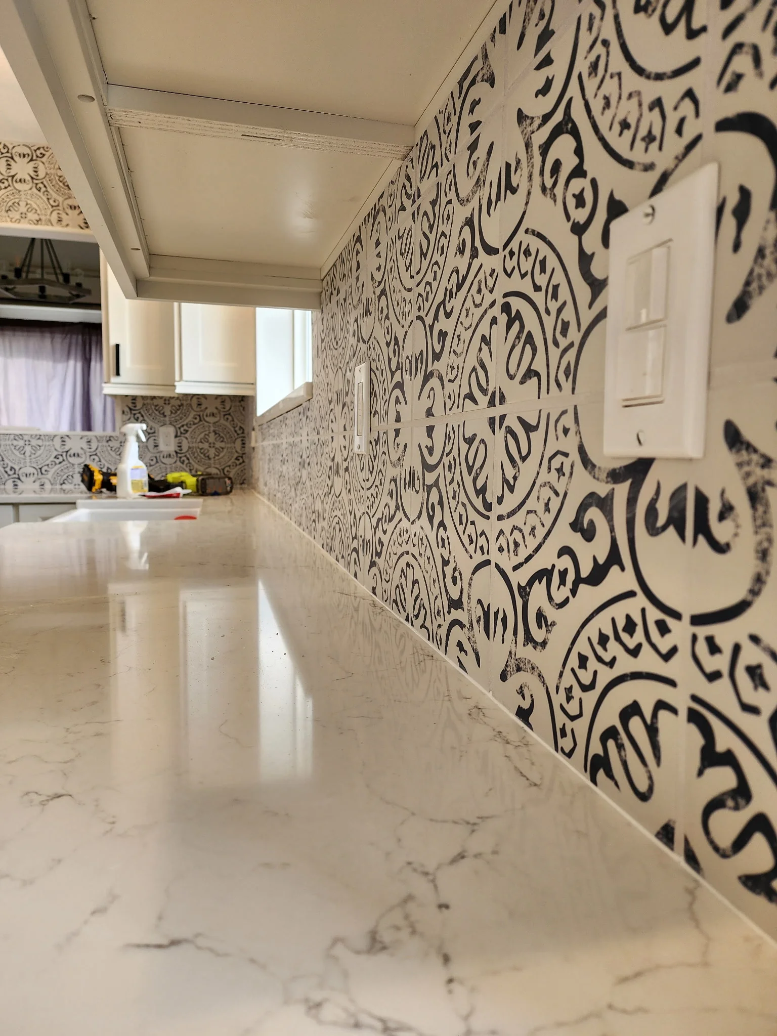 Kitchen with black ornate patterned tile backsplash, marble flooring, white cabinetry, and recessed lighting