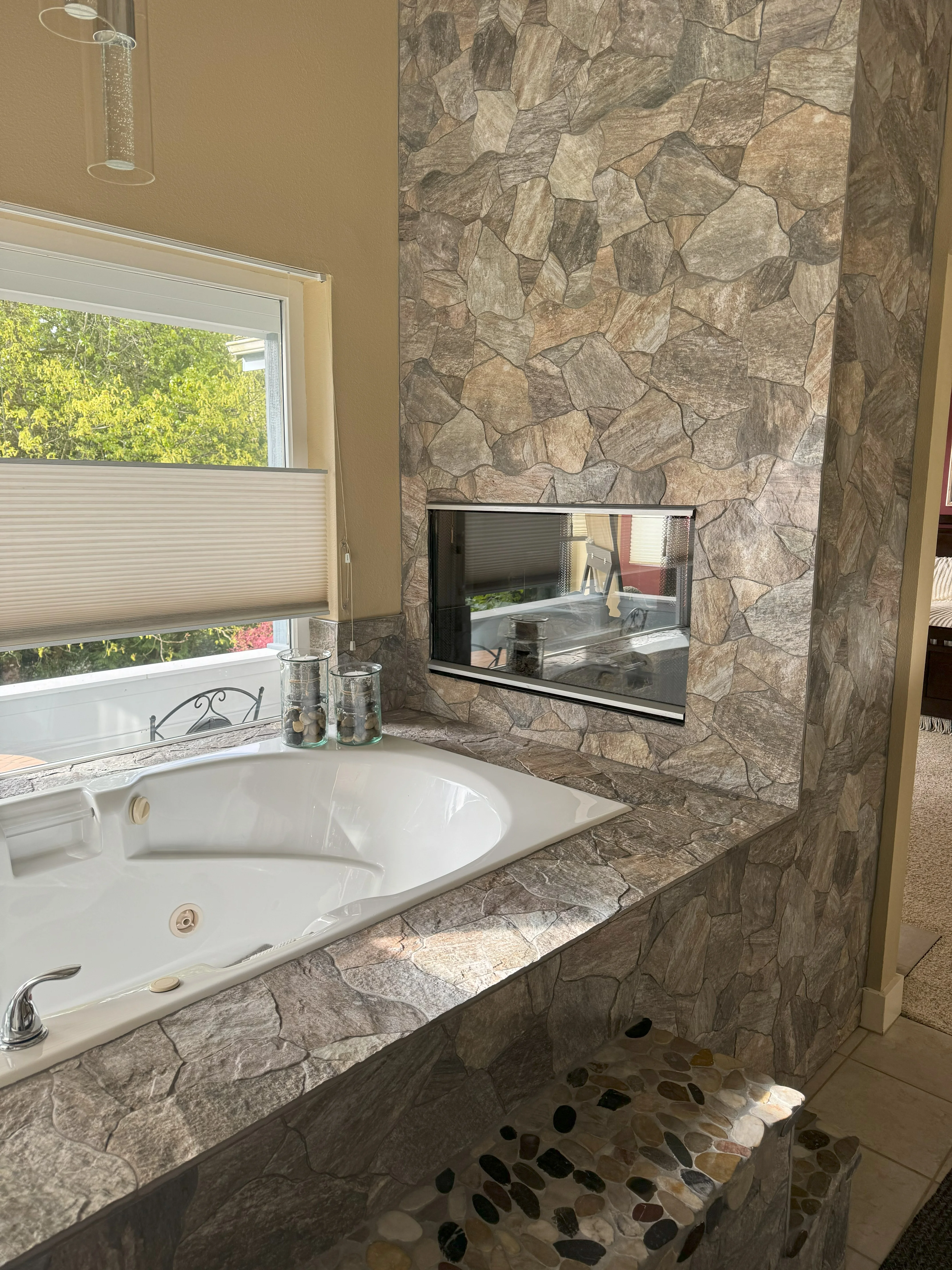 Master bathroom with stacked stone walls, white soaking tub, granite counters, and river rock floor accents