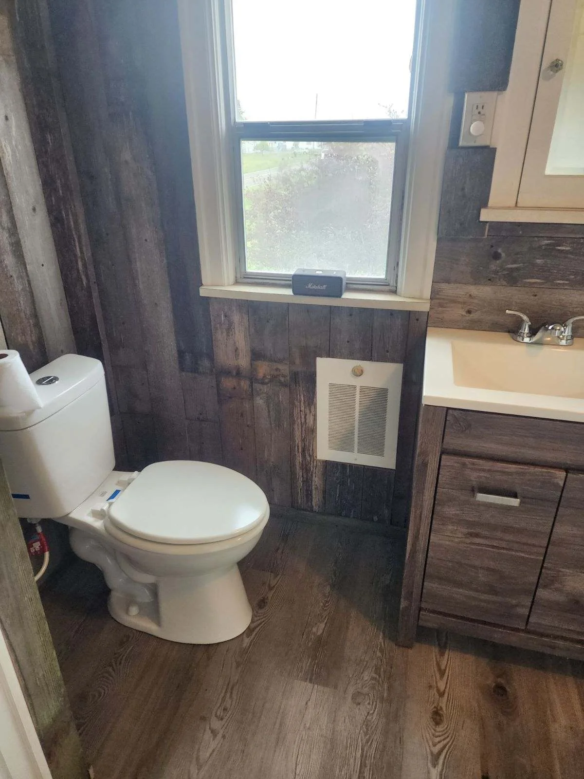 Restored bathroom with dark wood flooring, wood-paneled walls, white toilet and sink, wooden vanity cabinet