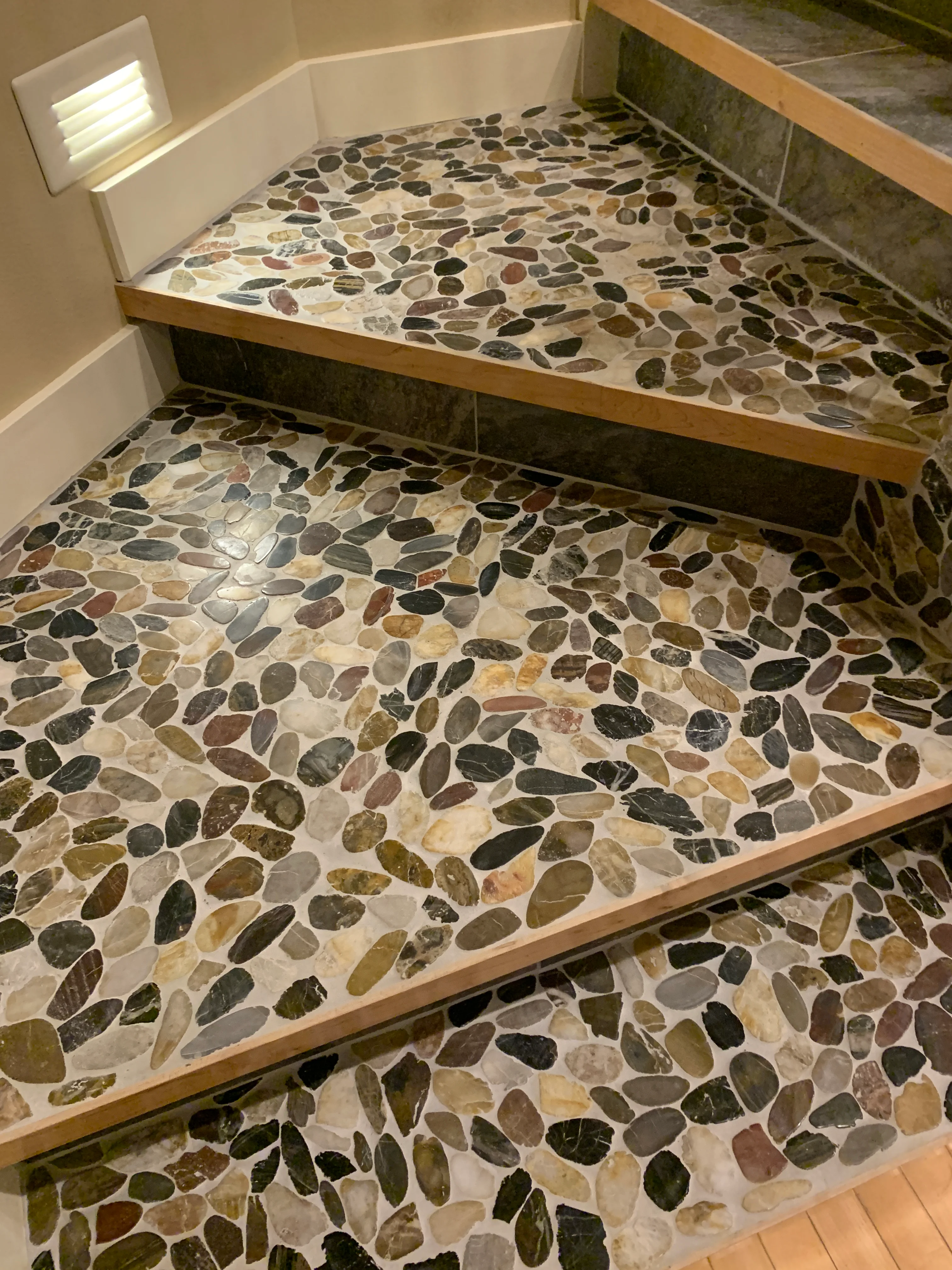 Multi-level pebble tile shower with natural stone flooring and wood trim framing
