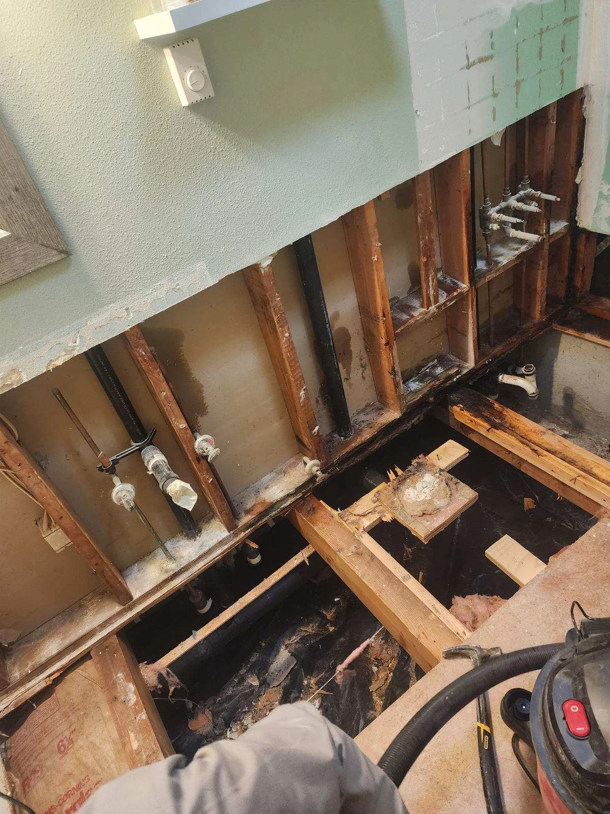Water-damaged wall cavity with exposed wood framing, wet insulation, and visible plumbing lines requiring mitigation