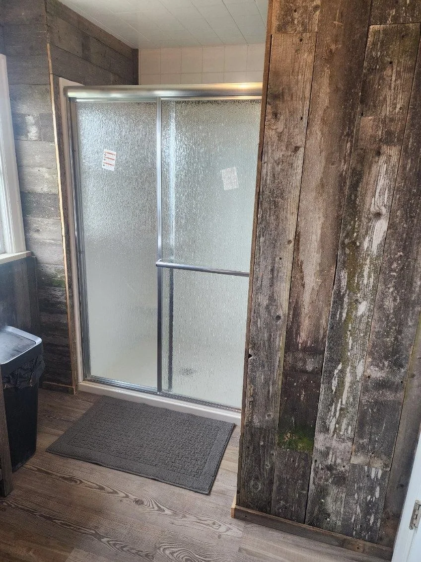 Framed shower enclosure with textured glass doors, distressed wood wall paneling, and vinyl plank flooring
